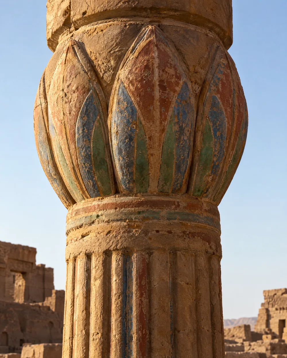 A carved lotus-bud capital crowning a fluted sandstone column, with traces of its old paint